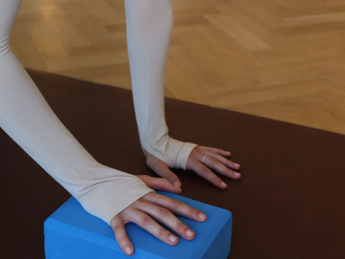 Manos apoyadas en el suelo y sobre un bloque durante una clase de Pilates Mat